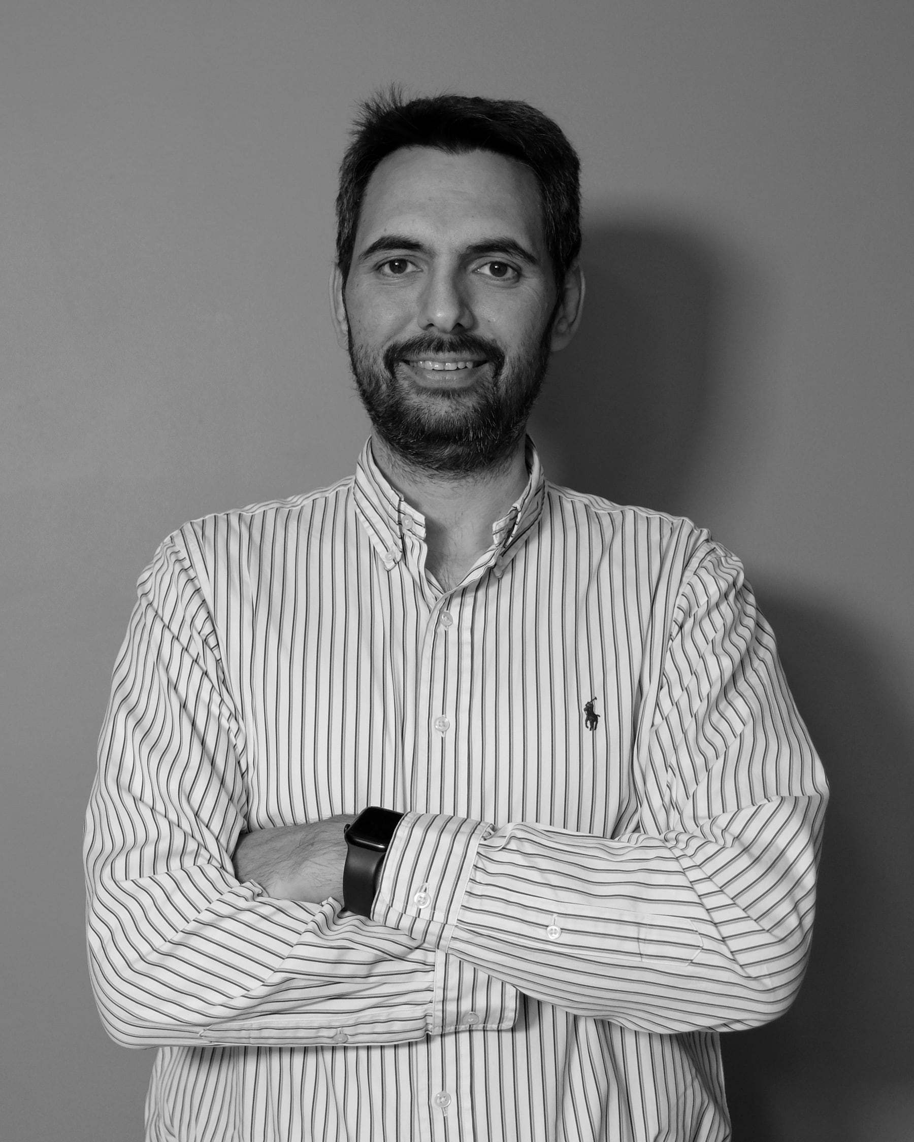 Hamdi Uğur in a striped shirt, arms crossed and smiling; black-and-white portrait