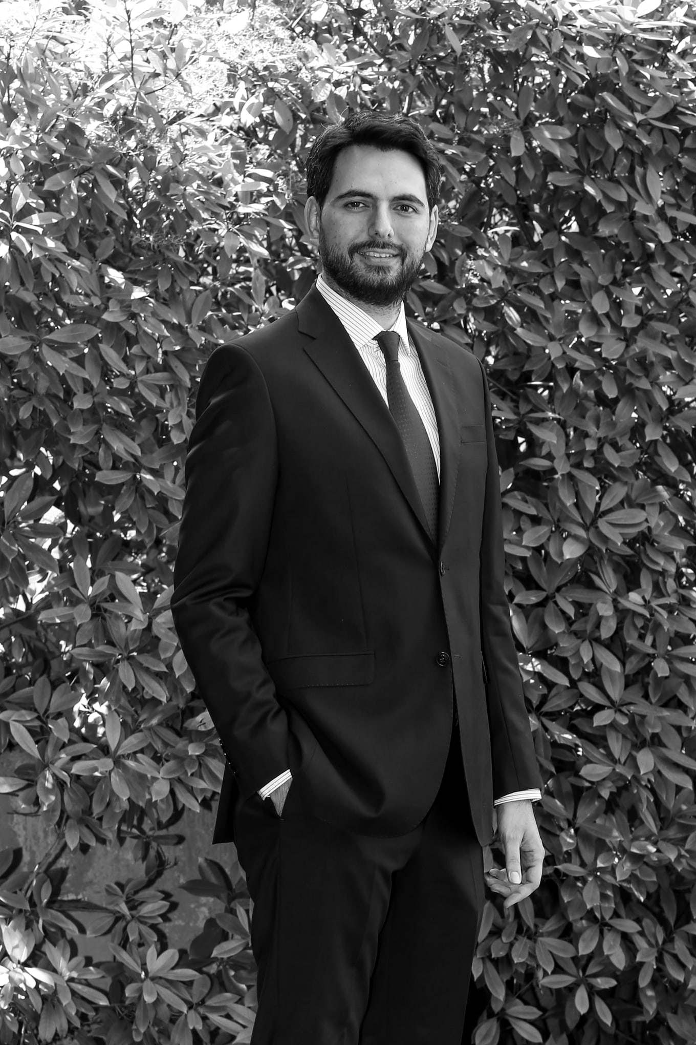 Hamdi Uğur standing in a suit in front of ivy; black-and-white portrait
